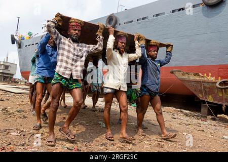 Dhaka, Dhaka, Bangladesh. 9 août 2023. Un groupe de porteurs transporte une lourde plaque d'acier de 250 kg dans un chantier naval sur la rive de la rivière Buriganga, à Keraniganj, près de Dhaka, Bangladesh. Des douzaines de chantiers navals occupant 30,96 acres de la côte de Buriganga sont en activité depuis 50 ans. Il est principalement utilisé pour la fixation et la réparation de vieux navires, et construire dans de nouveaux navires. Les travailleurs travaillent dans le chantier naval sans casques, masques faciaux ou chaussures de sécurité. Ils travaillent dur toute la journée, mais reçoivent toujours un salaire minimum. Avec un nombre croissant de commandes des acheteurs locaux et mondiaux, le shipbuil Banque D'Images