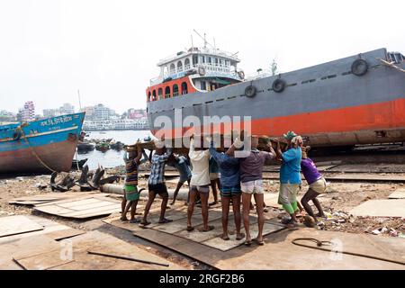 Dhaka, Dhaka, Bangladesh. 9 août 2023. Un groupe de porteurs transporte une lourde plaque d'acier de 250 kg dans un chantier naval sur la rive de la rivière Buriganga, à Keraniganj, près de Dhaka, Bangladesh. Des douzaines de chantiers navals occupant 30,96 acres de la côte de Buriganga sont en activité depuis 50 ans. Il est principalement utilisé pour la fixation et la réparation de vieux navires, et construire dans de nouveaux navires. Les travailleurs travaillent dans le chantier naval sans casques, masques faciaux ou chaussures de sécurité. Ils travaillent dur toute la journée, mais reçoivent toujours un salaire minimum. Avec un nombre croissant de commandes des acheteurs locaux et mondiaux, le shipbuil Banque D'Images