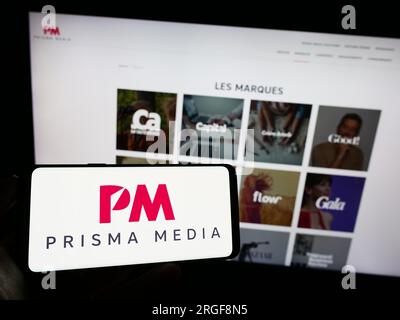 Personne tenant un téléphone portable avec le logo de la maison d'édition française Prisma Media sur l'écran devant la page Web de l'entreprise. Concentrez-vous sur l'affichage du téléphone. Banque D'Images