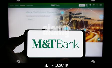 Personne tenant le téléphone portable avec le logo de la société financière américaine MT Bank Corporation sur l'écran devant la page Web de l'entreprise. Concentrez-vous sur l'affichage du téléphone. Banque D'Images