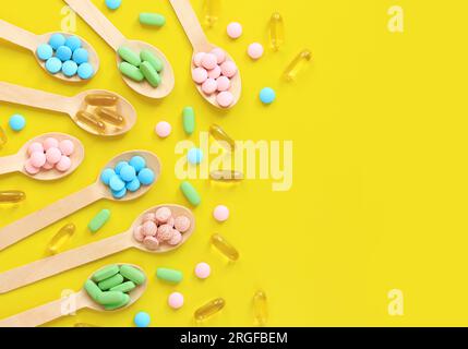 Vitamines de différentes couleurs dans des cuillères en bois sur fond jaune. Vue de dessus des pilules brillantes dispersées. Industrie pharmaceutique. Soins de santé et médicaments Banque D'Images