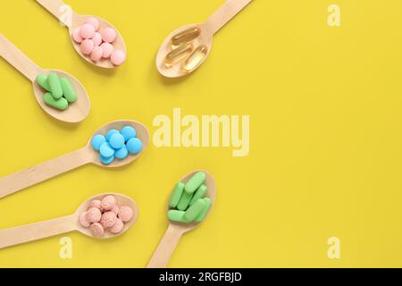 Vitamines sur fond jaune, vue de dessus. Pilules de différentes couleurs dans des cuillères en bois, pose à plat. Médicaments, vitamines et compléments alimentaires Banque D'Images