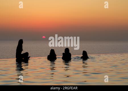 IOS, Grèce - 17 août 2018 : amis dans une piscine qui surplombe la mer Égée en regardant un coucher de soleil à couper le souffle à iOS cyclades Grèce Banque D'Images