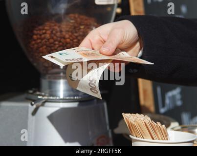 Une main de femme tenant un tas de billets de banque en papier dans un stand de café dans un marché extérieur. Banque D'Images