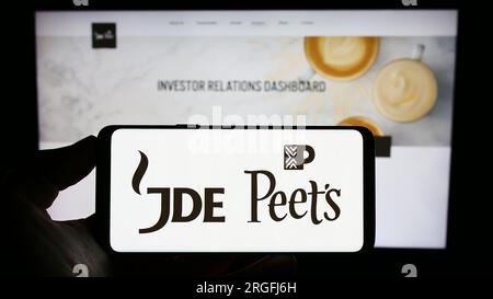 Personne tenant le téléphone cellulaire avec le logo de la société de boissons JDE Peet's N.V. sur l'écran devant la page Web de l'entreprise. Concentrez-vous sur l'affichage du téléphone. Banque D'Images
