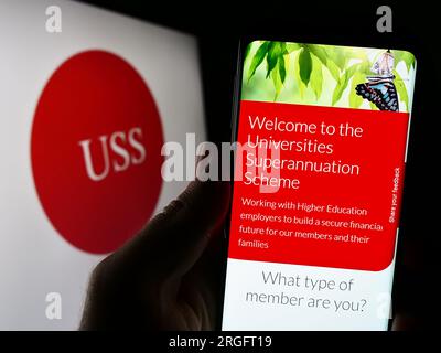 Personne tenant un smartphone avec le site Web de Universities Superannuation Scheme (USS) sur l'écran devant le logo. Concentrez-vous sur le centre de l'écran du téléphone. Banque D'Images
