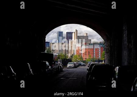 Voitures garées dans une rue et sous l'arche d'un viaduc de chemin de fer avec une ligne d'horizon du centre-ville de grands bâtiments dans le centre-ville de Manchester, en Angleterre. Banque D'Images