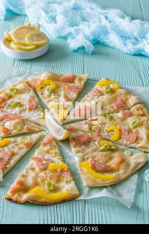 Tarte flambee avec saumon, poivre jaune et oignons verts sur fond bleu clair, verticale Banque D'Images