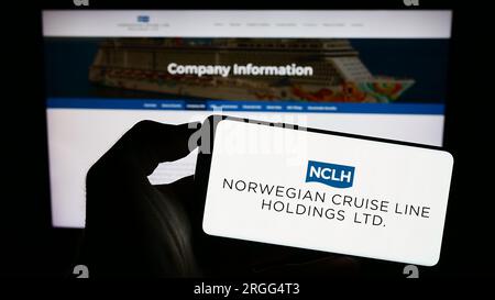 Personne tenant un smartphone avec le logo de la société Norwegian Cruise Line Holdings Ltd. Sur l'écran devant le site Web. Concentrez-vous sur l'affichage du téléphone. Banque D'Images