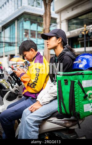 Un coursier thaïlandais est assis avec son amie sur son vélo en prenant une pause sur Sala Daeng Rd. Bangkok, Thaïlande. Banque D'Images