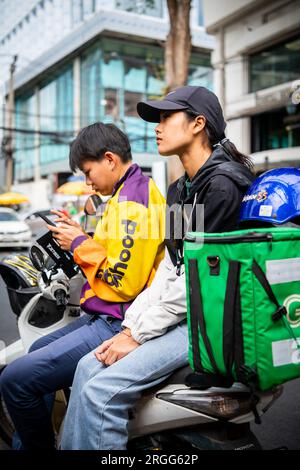 Un coursier thaïlandais est assis avec son amie sur son vélo en prenant une pause sur Sala Daeng Rd. Bangkok, Thaïlande. Banque D'Images