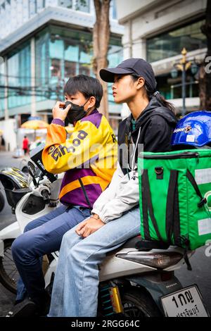 Un coursier thaïlandais est assis avec son amie sur son vélo en prenant une pause sur Sala Daeng Rd. Bangkok, Thaïlande. Banque D'Images