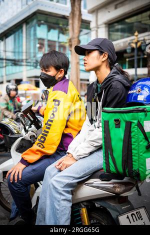 Un coursier thaïlandais est assis avec son amie sur son vélo en prenant une pause sur Sala Daeng Rd. Bangkok, Thaïlande. Banque D'Images