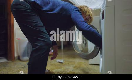 Une femme âgée mettant des vêtements dans la machine à laver. Scène domestique d'une personne effectuant une routine d'activité ménagère Banque D'Images