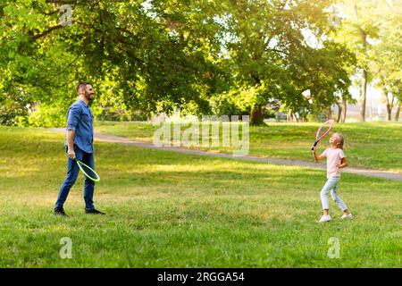 Passe-temps en famille. Vue latérale de papa jouant au badminton avec sa fille, tenant des raquettes et utilisant un grand volant Banque D'Images