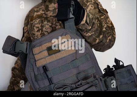 Soldat ukrainien dans le camouflage non formé pixel militaire avec gilet pare-balles gris dans une main et bannière de drapeau de l'Ukraine. Banque D'Images