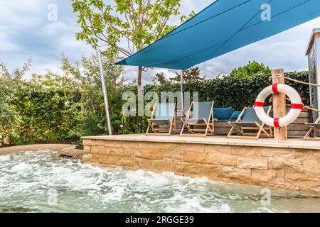 Terrasse avec chaises longues près du bain à remous intégré moderne. Piscine bouillonnante, espace spa Banque D'Images