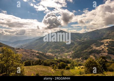 Vue panoramique sur la chaîne de montagnes et la vallée avec arbres verts et prairie verdoyante sous ciel bleu nuageux en plein jour Banque D'Images