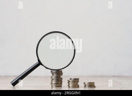 Une pile de pièces de monnaie en métal et une loupe en plastique sur fond blanc. Le concept d'augmentation des impôts, des subventions Banque D'Images