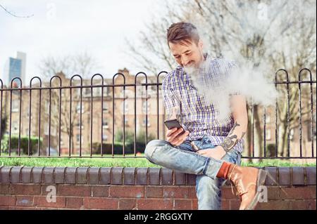 Adolescent fumer cigarette électronique dans park Banque D'Images