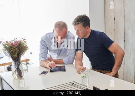 Gay couple using digital tablet in kitchen Banque D'Images