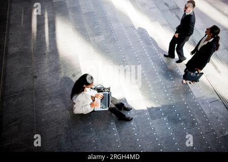 Vue à angle élevé de femme d'affaires utilisant un ordinateur portable sur l'escalier Banque D'Images