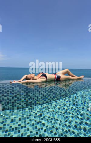 Jeune femme gisant sur le bord de piscine par mer Banque D'Images