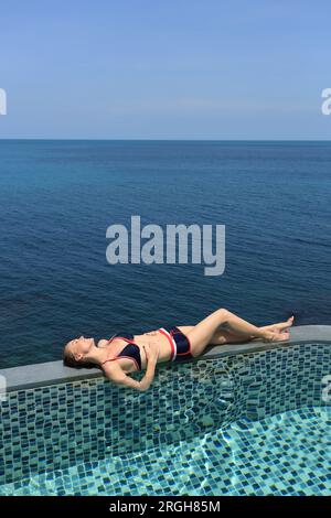 Jeune femme gisant sur le bord de piscine par mer Banque D'Images