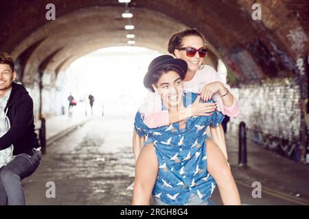 Teenage boy giving girlfriend piggyback ride in tunnel Banque D'Images