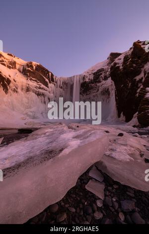 Grande perspective de Skogafoss avec des floes de glace au premier plan et beau ciel rouge. Banque D'Images