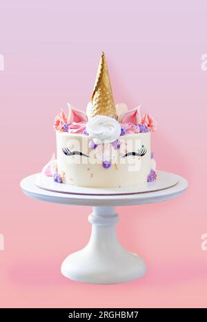 Magnifique gâteau licorne avec corne de gaufre dorée, cils et glaçage au fromage à la crème sur fond rose festif Banque D'Images