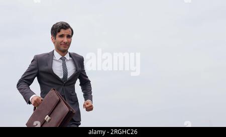 Photo de studio d'un homme d'affaires mature courant avec une mallette isolée contre le ciel. Banque D'Images