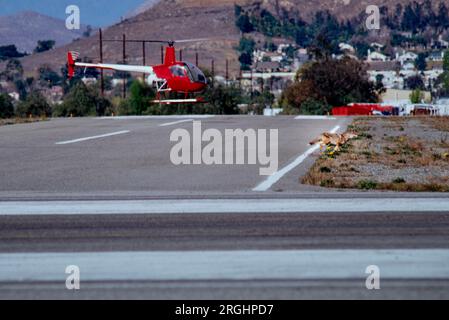 Un coyote traverse une voie de circulation alors qu'un hélicoptère décolle de l'aéroport de Riverside à Riverside, en Californie. Banque D'Images