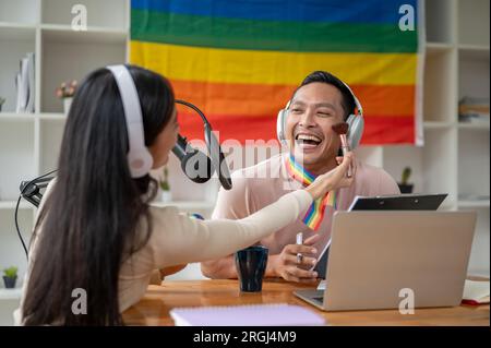 Un podcasteur ou animateur de radio gay asiatique attrayant et joyeux est composé par une invitée féminine dans son émission de radio. Banque D'Images