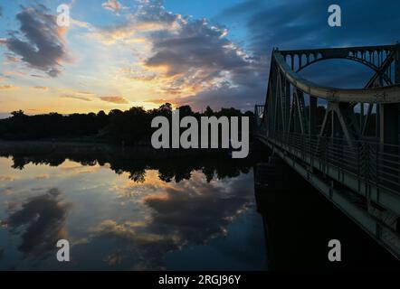 Potsdam, Allemagne. 10 août 2023. Le soleil se lève derrière le pont Glienicker, qui traverse la rivière Havel. Le pont à la frontière de la ville entre Potsdam et Berlin est un symbole pour surmonter la division entre l'est et l'Ouest. Cette année encore, de nombreux événements du 13 août commémorent la construction du mur et la division de l'Allemagne. Crédit : Soeren Stache/dpa/Alamy Live News Banque D'Images