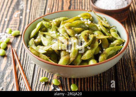 Apéritif japonais de haricots edamame frits assaisonnés de gros gros gros sel de mer sur une assiette sur la table. Horizontal Banque D'Images