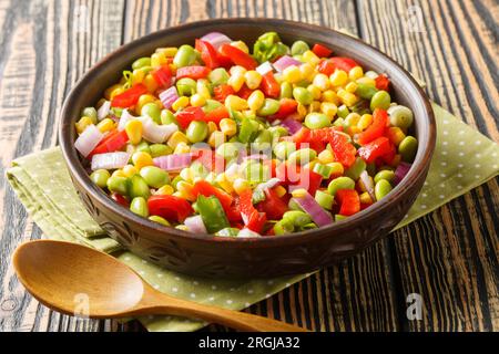 Salade fraîche avec du soja vert, des poivrons, des grains de maïs, des tomates et des oignons en gros plan dans un bol sur la table. Horizontal Banque D'Images