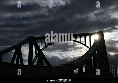 Potsdam, Allemagne. 10 août 2023. Le soleil se lève derrière le pont Glienicker, qui traverse la rivière Havel. Le pont à la frontière de la ville entre Potsdam et Berlin est un symbole pour surmonter la division entre l'est et l'Ouest. Cette année encore, de nombreux événements du 13 août commémorent la construction du mur et la division de l'Allemagne. Crédit : Soeren Stache/dpa/Alamy Live News Banque D'Images