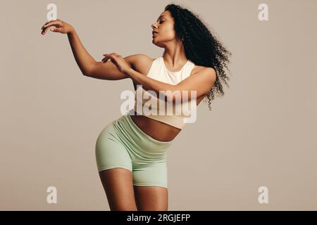 Jeune femme confiante dansant dans des vêtements de fitness, mettant en valeur son physique flexible. Femme avec un corps tonique s'exprimant à travers un effort Banque D'Images