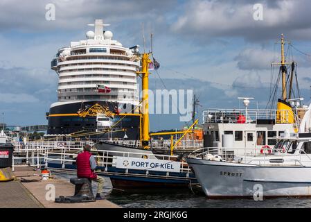 Kiel, Deutschland, août 2023 Hafenimpressionnen Ein Angler auf einem Poller am Museumshafen sitzend betrachtet die Disney Dream Banque D'Images