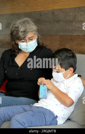 Latine femme, grand-mère et enfant 7 ans avec masque de protection utilisation clinique pour covid-19 dans la salle d'attente, nouvelle normale à l'aide de gel antibactérien Banque D'Images