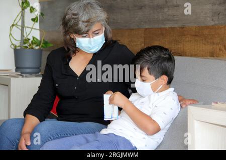 Latine femme, grand-mère et enfant 7 ans avec masque de protection utilisation clinique pour covid-19 dans la salle d'attente, nouvelle normale à l'aide de gel antibactérien Banque D'Images