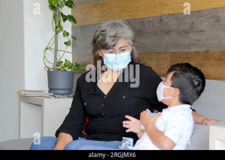 Latine femme, grand-mère et enfant 7 ans avec masque de protection utilisation clinique pour covid-19 dans la salle d'attente, nouvelle normale à l'aide de gel antibactérien Banque D'Images