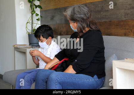 Latine femme, grand-mère et enfant 7 ans avec masque de protection utilisation clinique pour covid-19 dans la salle d'attente, nouvelle normale à l'aide de gel antibactérien Banque D'Images