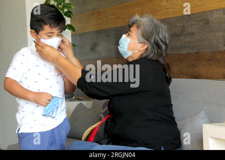 Latine femme, grand-mère et enfant 7 ans avec masque de protection utilisation clinique pour covid-19 dans la salle d'attente, nouvelle normale à l'aide de gel antibactérien Banque D'Images