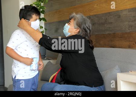 Latine femme, grand-mère et enfant 7 ans avec masque de protection utilisation clinique pour covid-19 dans la salle d'attente, nouvelle normale à l'aide de gel antibactérien Banque D'Images