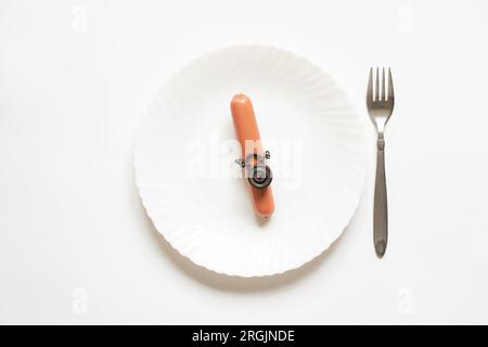 Saucisse sur une chaîne sous un cadenas sur une assiette et une fourchette à côté, rejet de la malbouffe, régime alimentaire Banque D'Images