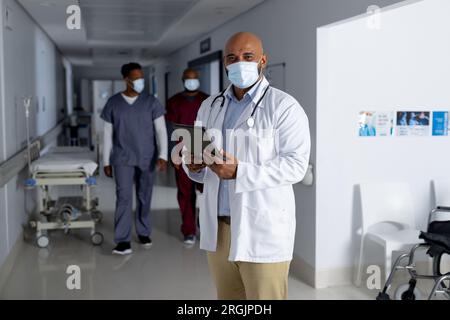 Portrait d'un médecin biracial portant un masque facial dans le couloir de l'hôpital Banque D'Images