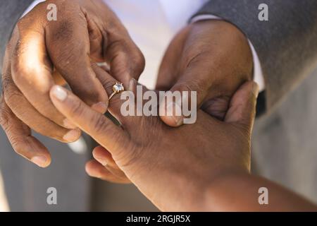 Mains du marié biracial senior mettant la bague de mariage sur le doigt de sa mariée Banque D'Images