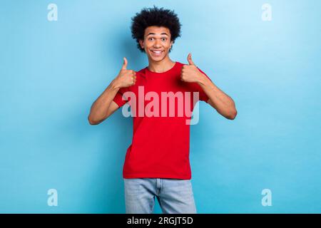 Portrait de joyeux drôle de cheveux bouclés jeune gars levez les doigts du pouce vers le haut d'accord exprès fond de couleur bleue isolé Banque D'Images